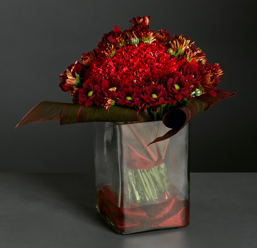 Scarlet carnations and crimson chrysanthemums in a glass cube